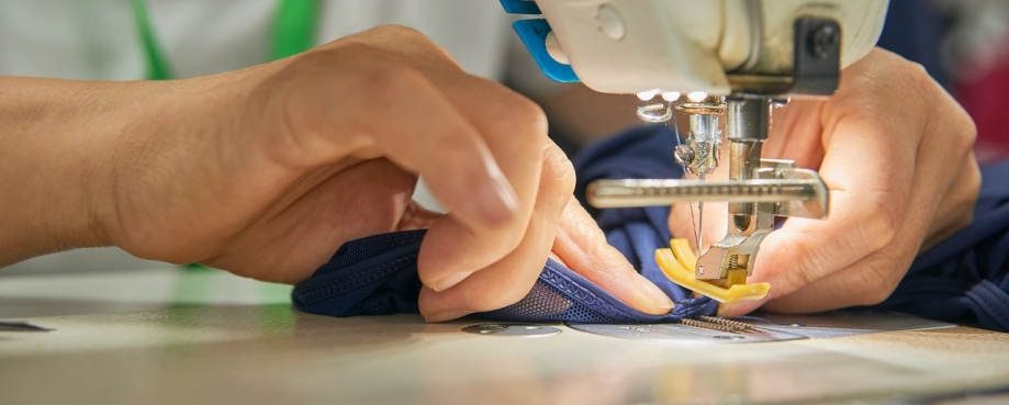 Hands feed fabric through a sewing machine. Photo credit: Shutterstock.