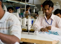 Male garment factory workers, sitting at sewing machines, India